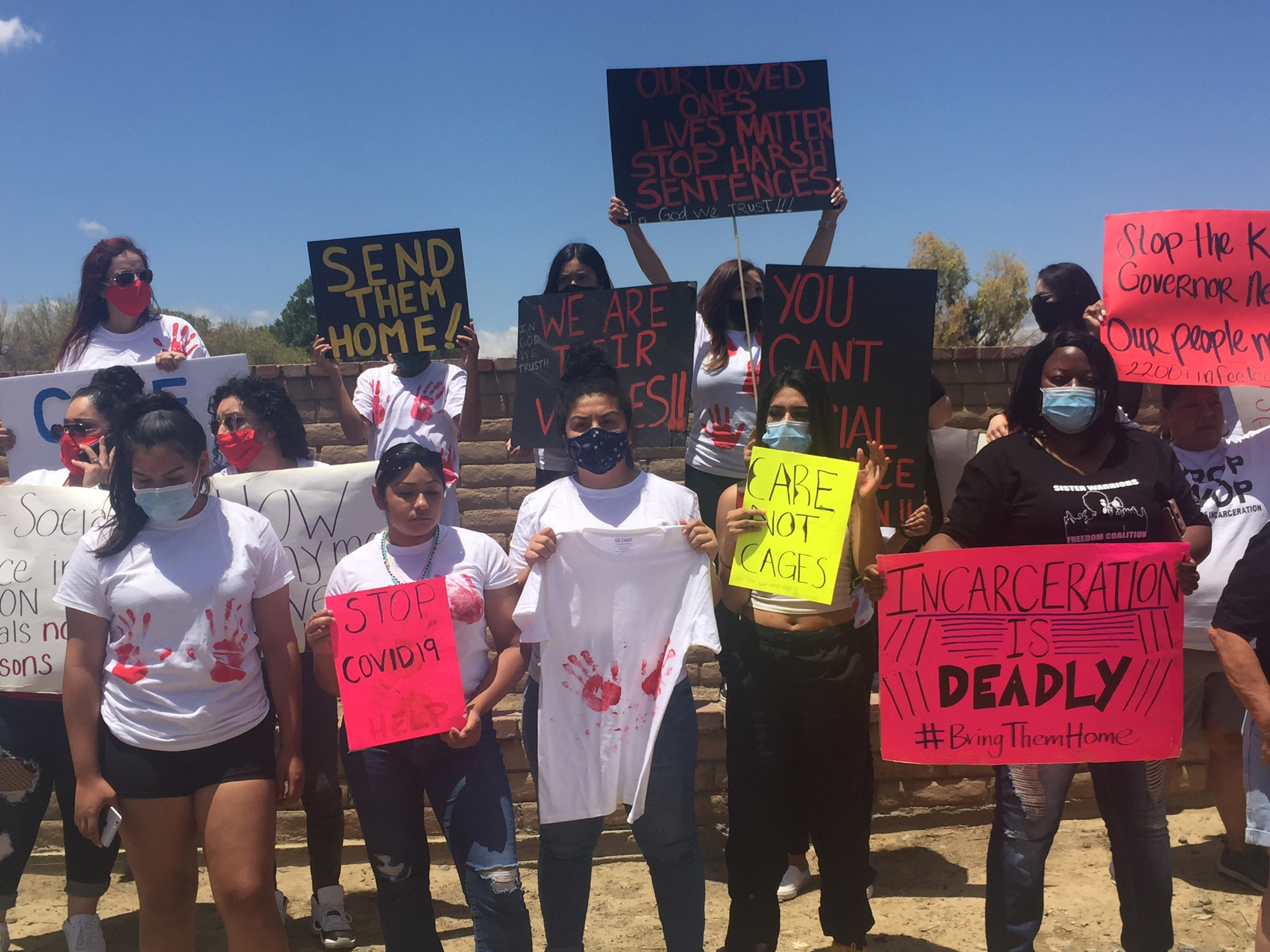 a dozen or so people hold bright colored signs to protest covid cases in prison
