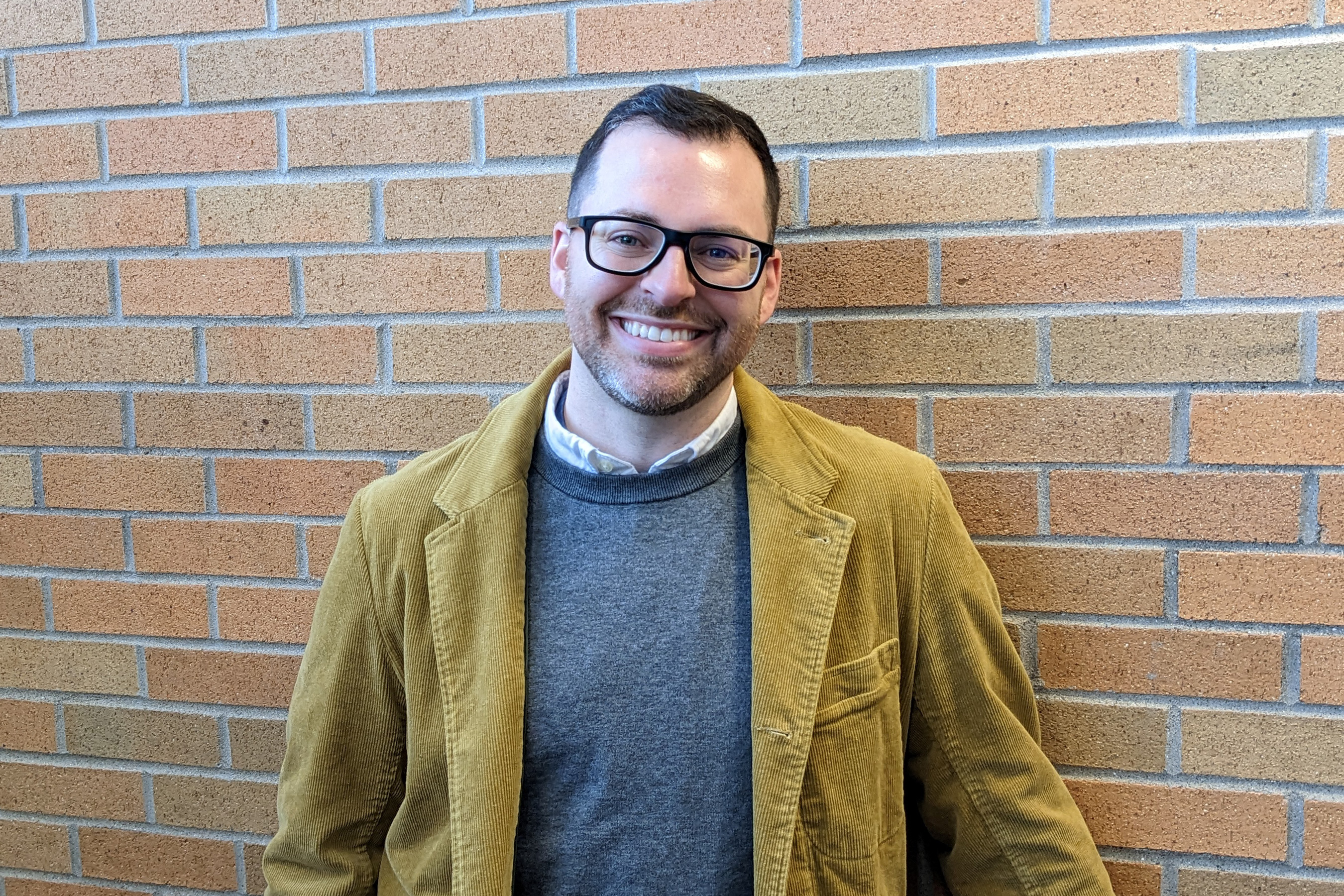A photo of a man posing for a portrait in front of a brick wall.