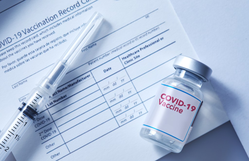 A vial of coronavirus vaccine on a vaccination record card with a syringe on the side.