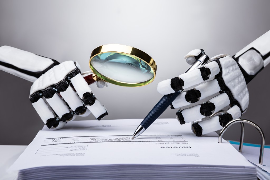 A pair of robot hands examines an invoice with a magnifying glass.