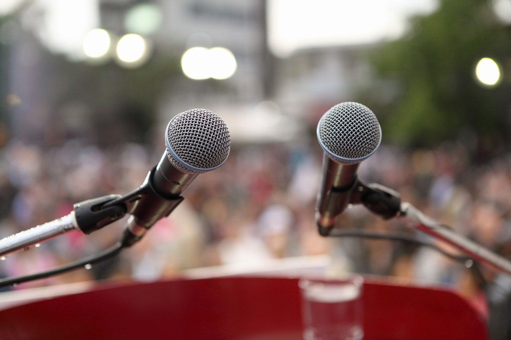 Two microphones are in frame with a crowd out of focus in the background.