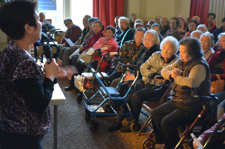 Qi Yu Xiao speaks to a group in the lobby of the Hotel Oakland, a low-income senior housing facility in downtown Oakland. (David Gorn/California Healthline)