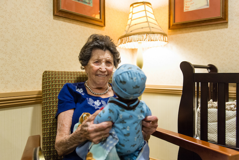 Vivian Guzofsky, 88, holds a baby at Sunrise Senior Living in Beverly Hills, California, on August 2, 2016. Some nursing homes are using a technique called doll therapy to ease anxiety among their residents with dementia. (Heidi de Marco/KHN)