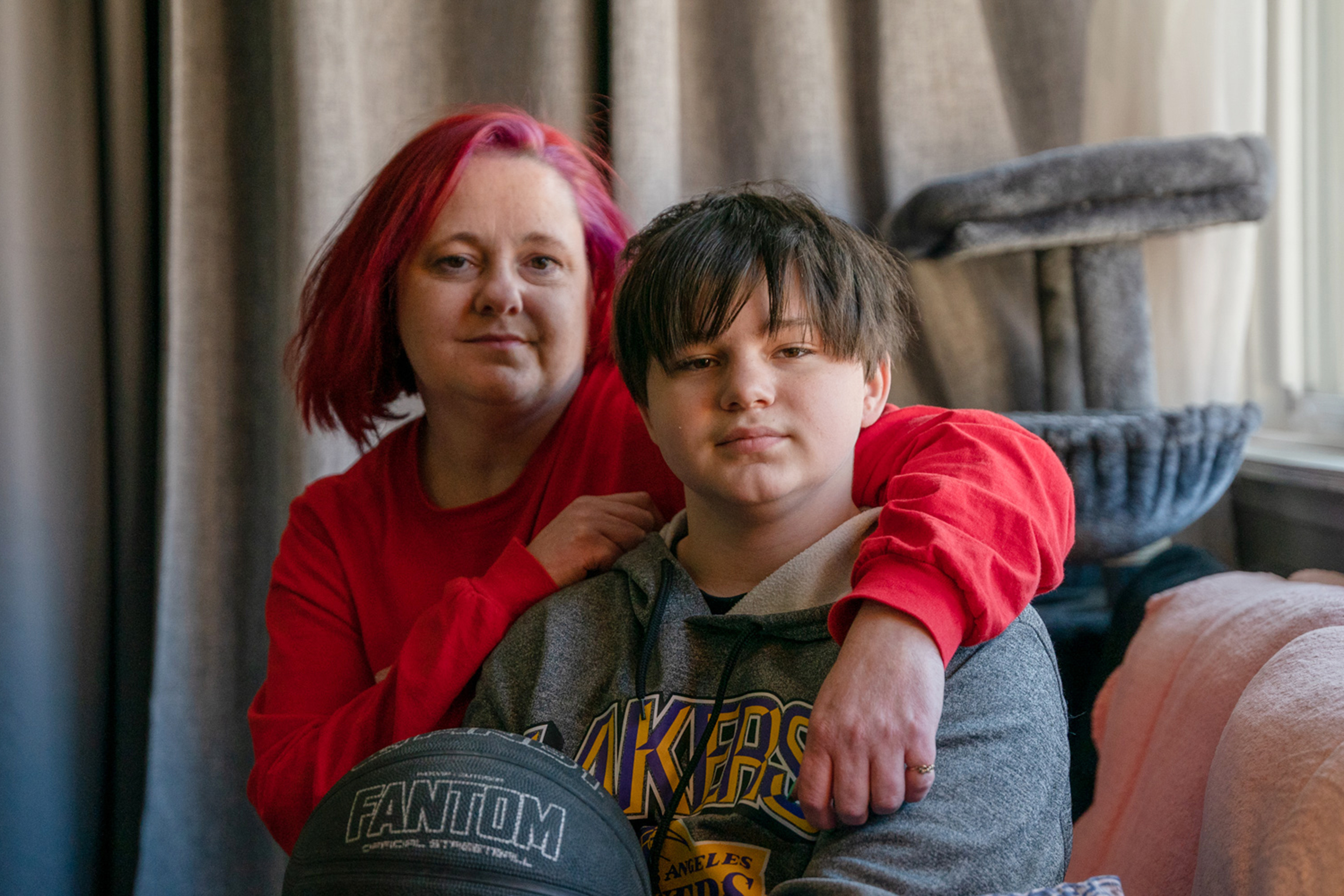 Stacey Whitford sits with her arms wrapped around her son as he sits in front of her.