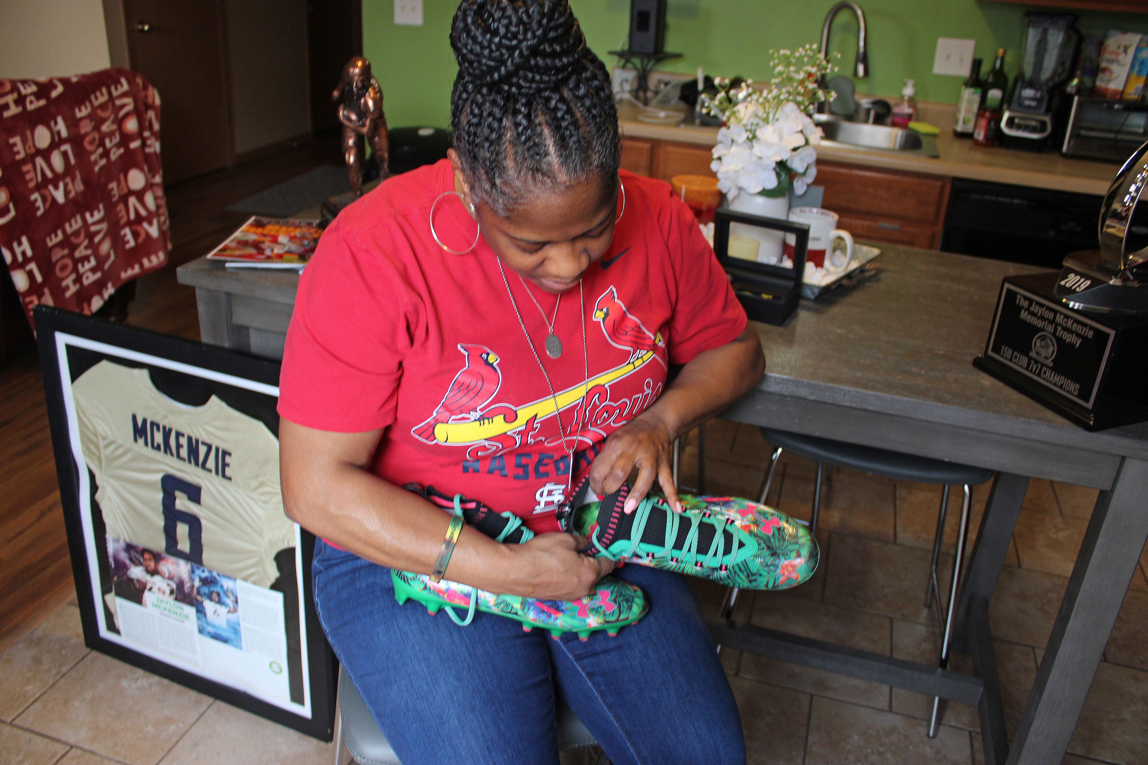 Sukeena Gunner is seen at her home, holding a pair of her son's football cleats and surrounded by a trophy and her son's jersey.