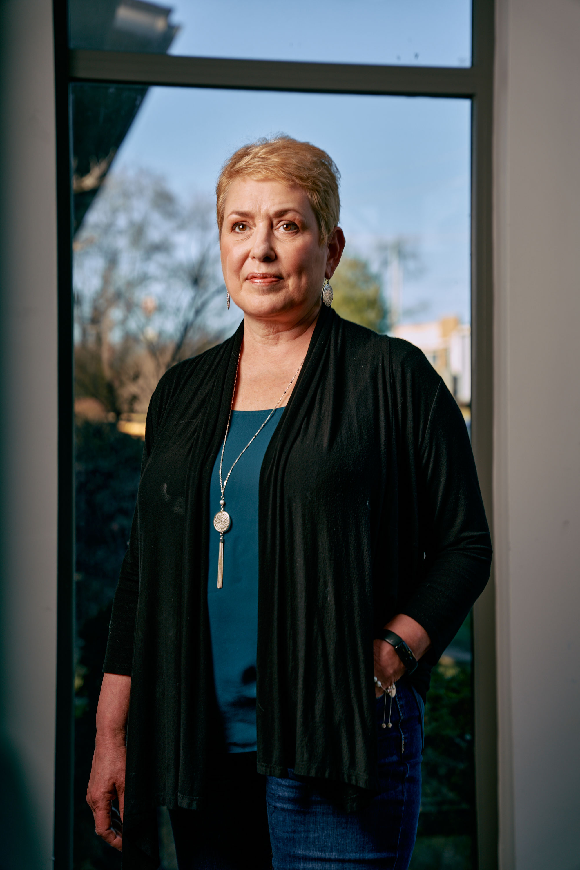 A woman stands in front of a window.