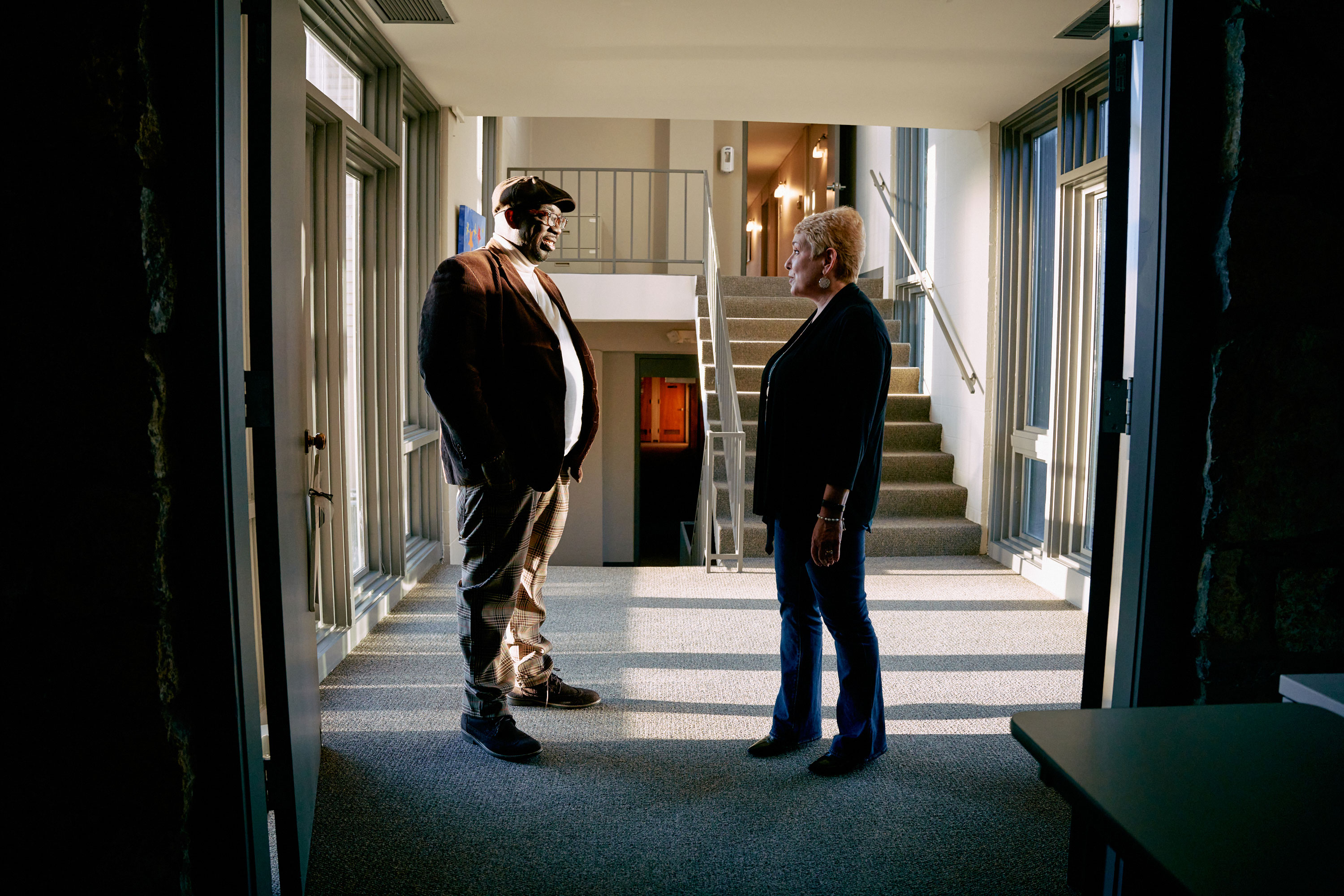 A man and a woman talk in a hallway.