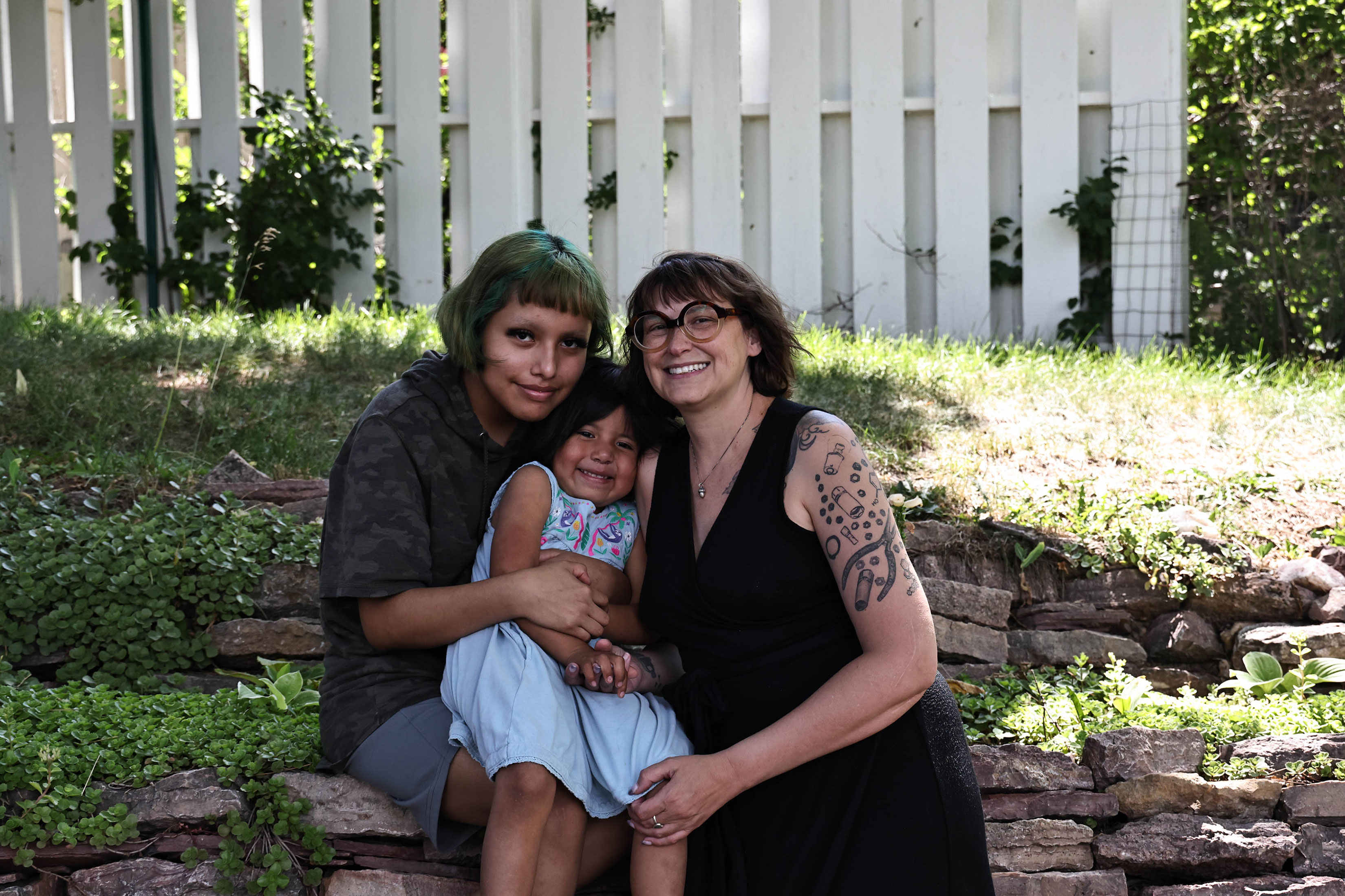 A smiling woman and two children pose together outside.