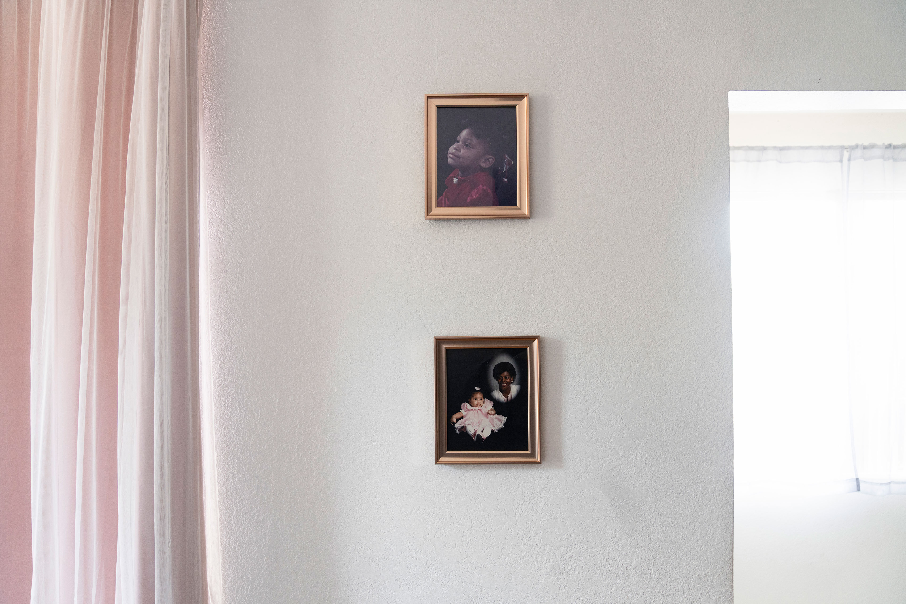 Two photos of a child a different ages in gold frames hang on an otherwise bare white wall.