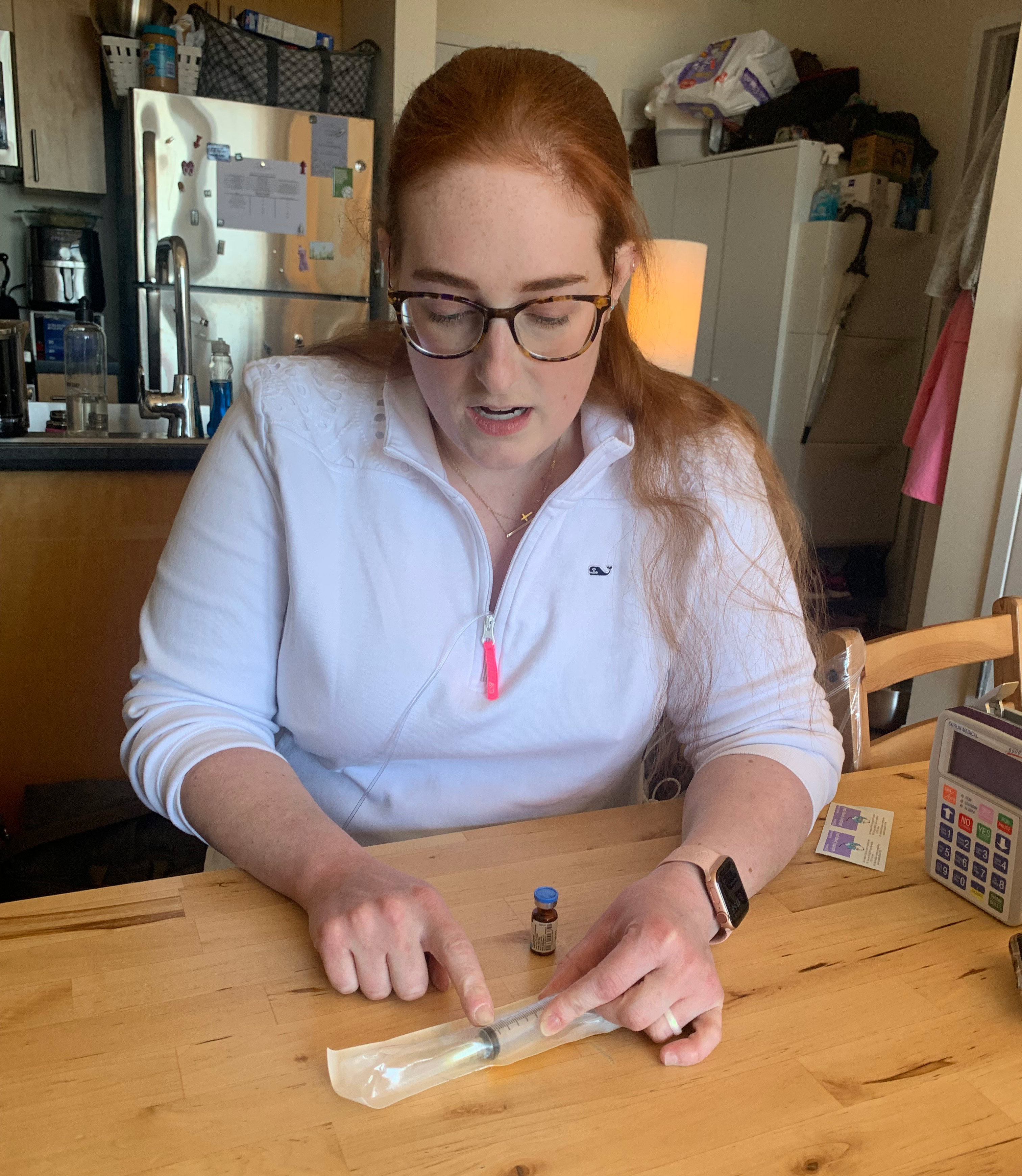 A photo shows Elizabeth Fisher Smith pointing to a syringe she uses for her medication.