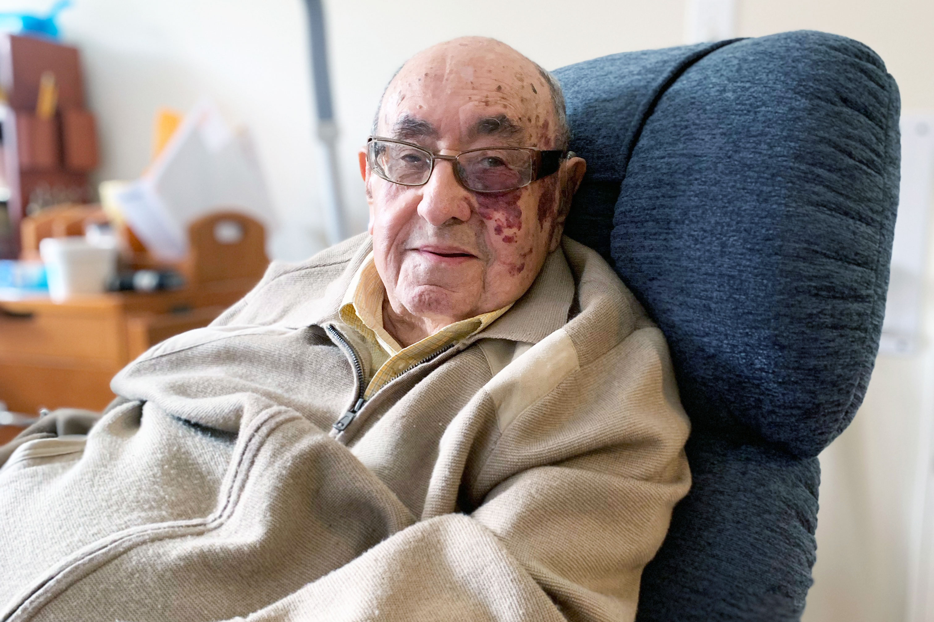 A photo shows Melvin Zax sitting at home.