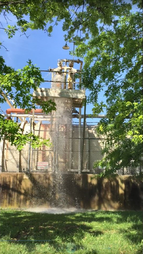 Water falls from a tank onto grass outside a wall.