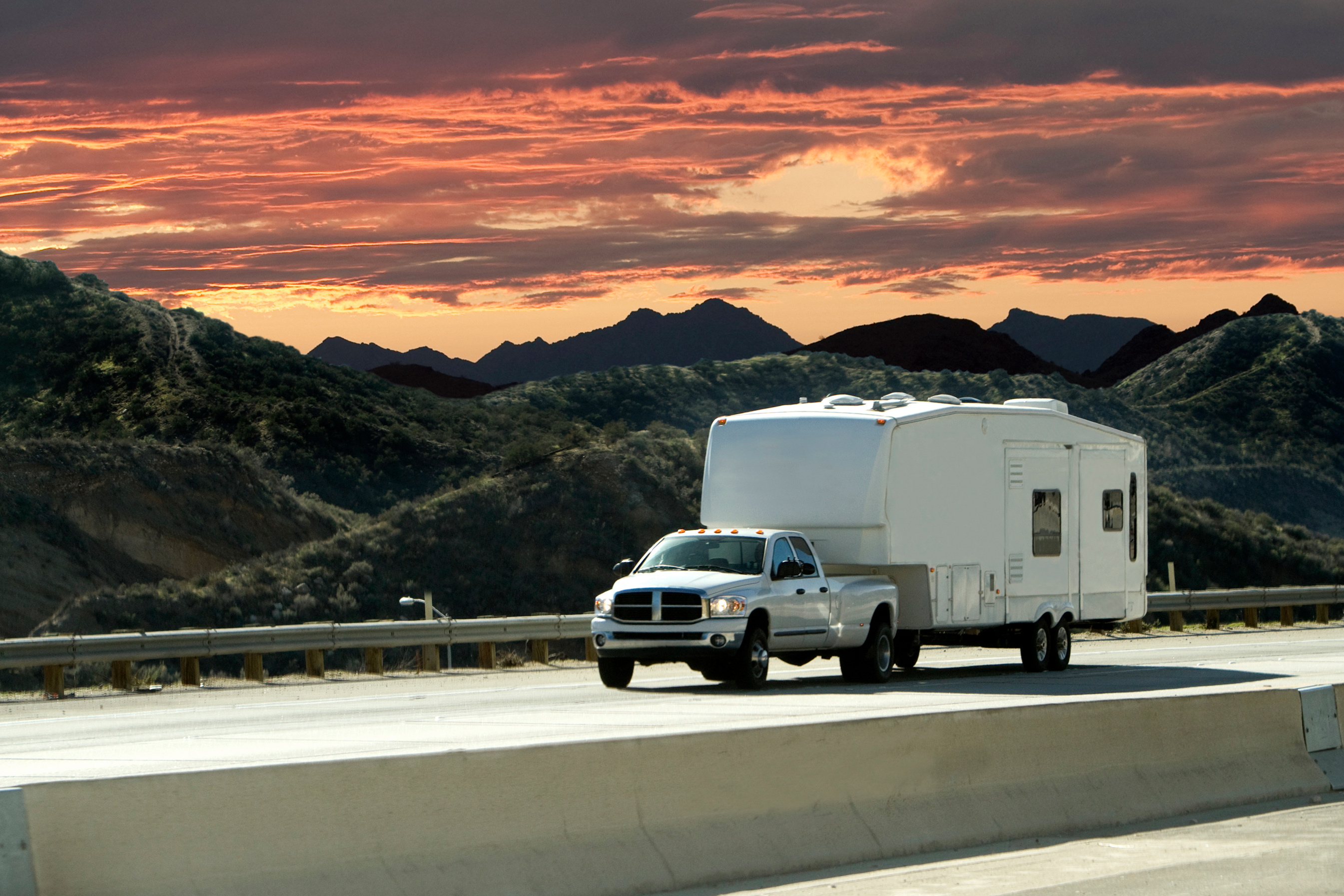 A photo of a truck pulling an RV trailer behind it driving on a highway.
