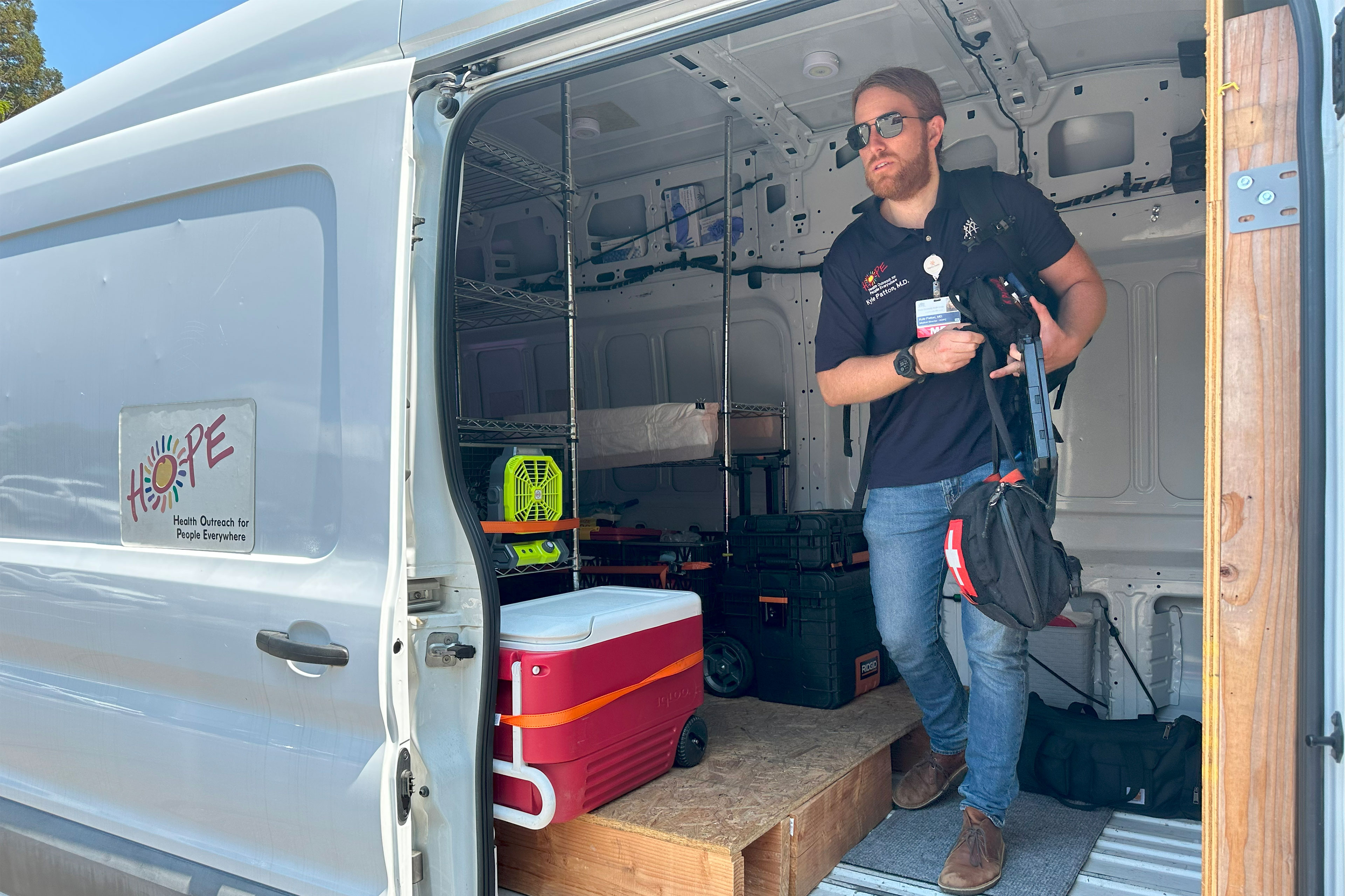 A man carrying bags several climbs out of van with "HOPE Human Outreach for People Everywhere" on the side.