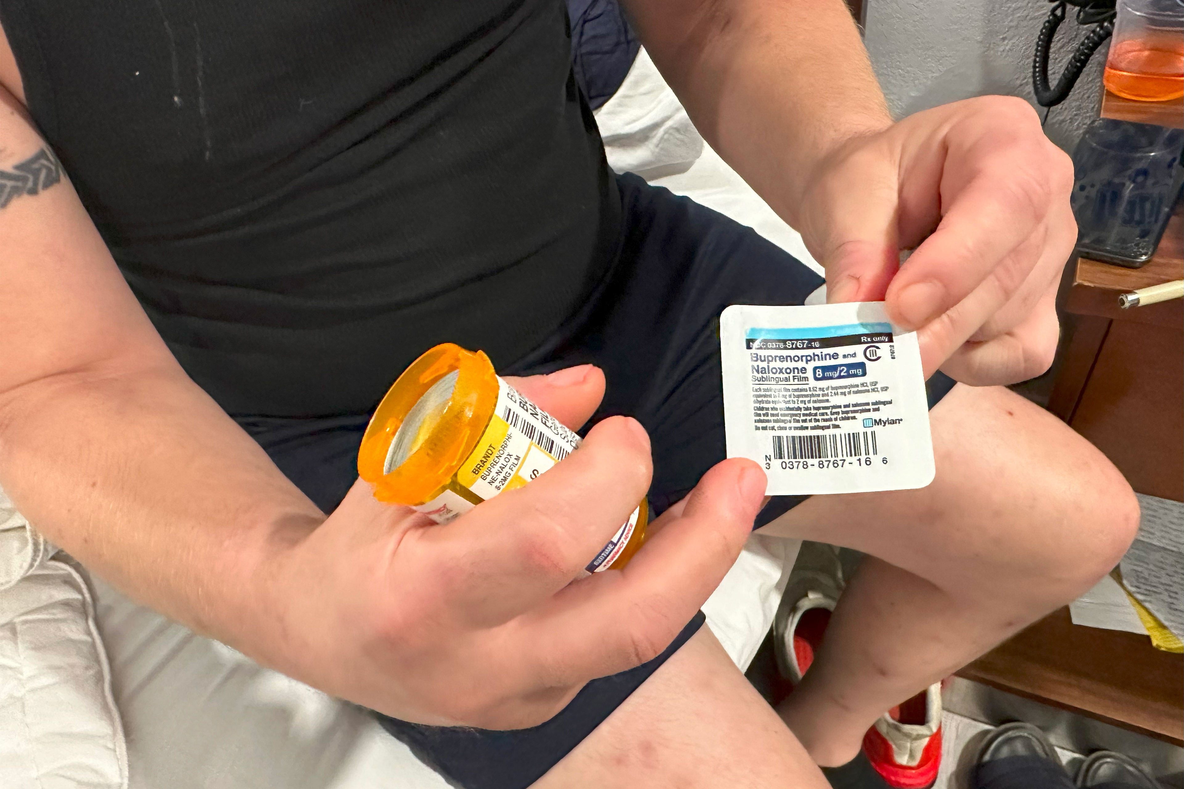 A close-up image a man's hand as he holds a prescription medication bottle and a packet containing a Suboxone strip.