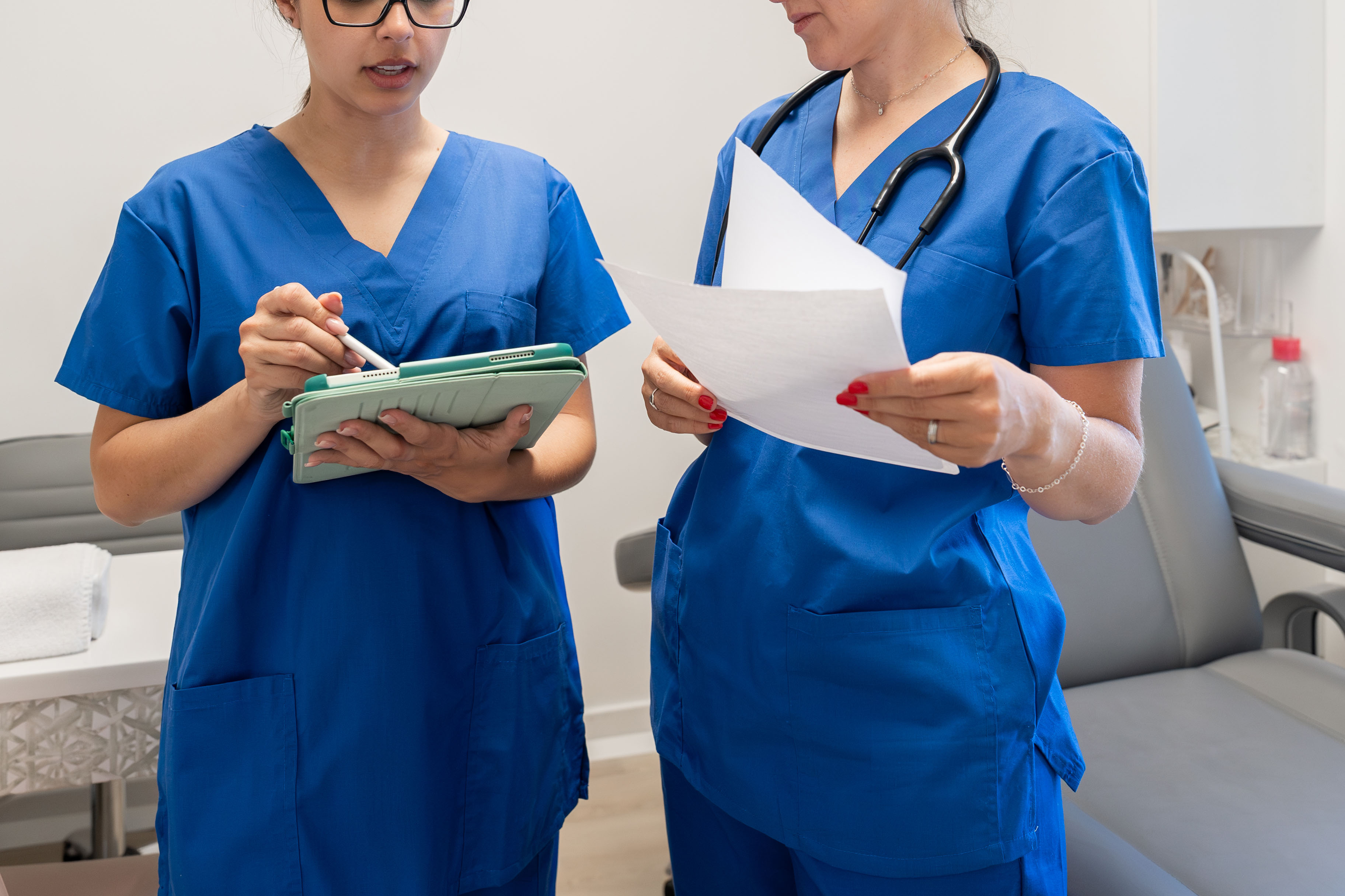 Two female health care providers stand side by side reviewing notes.