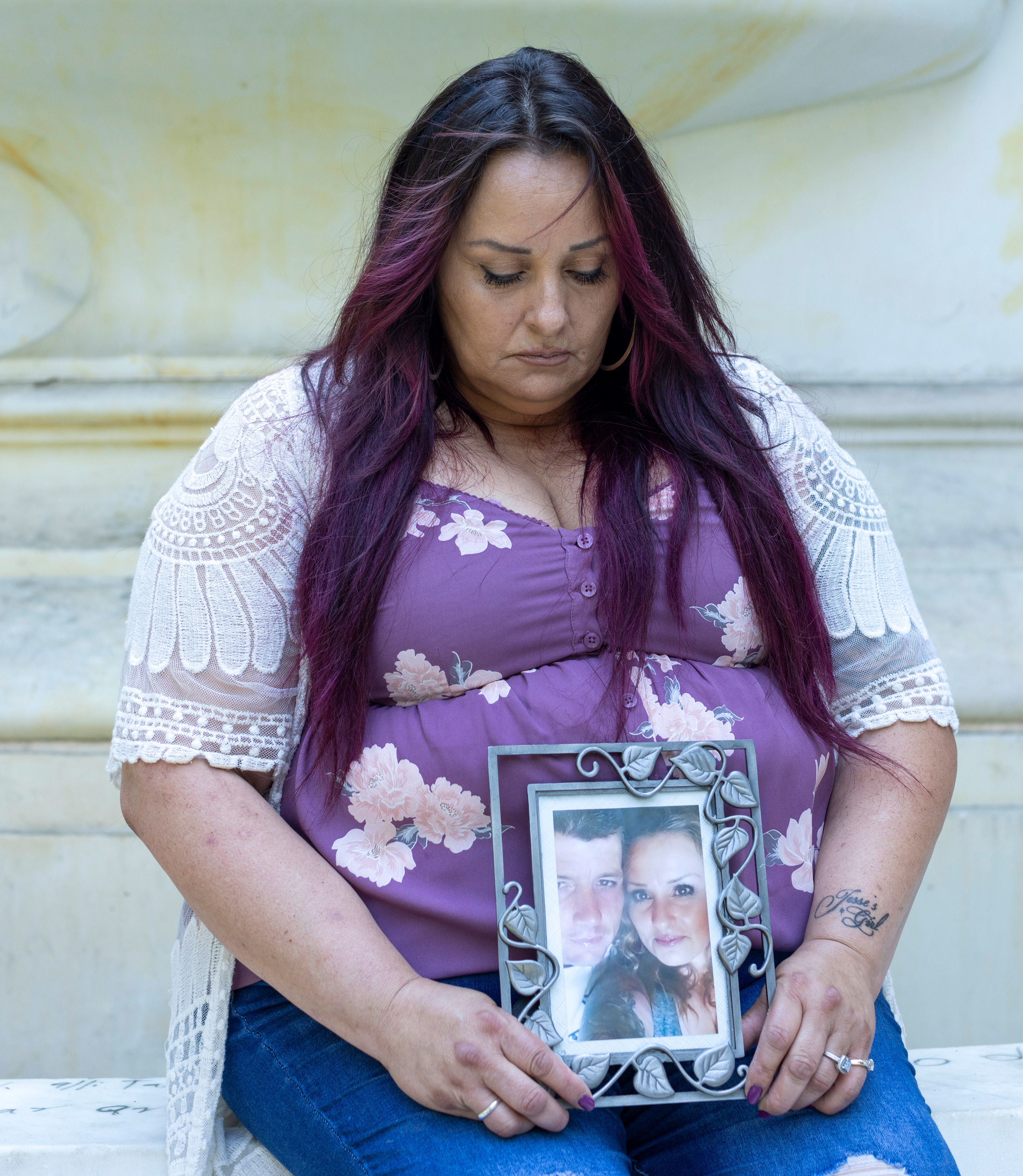 A portrait of woman seated, holding a photo of her deceased husband and herself.