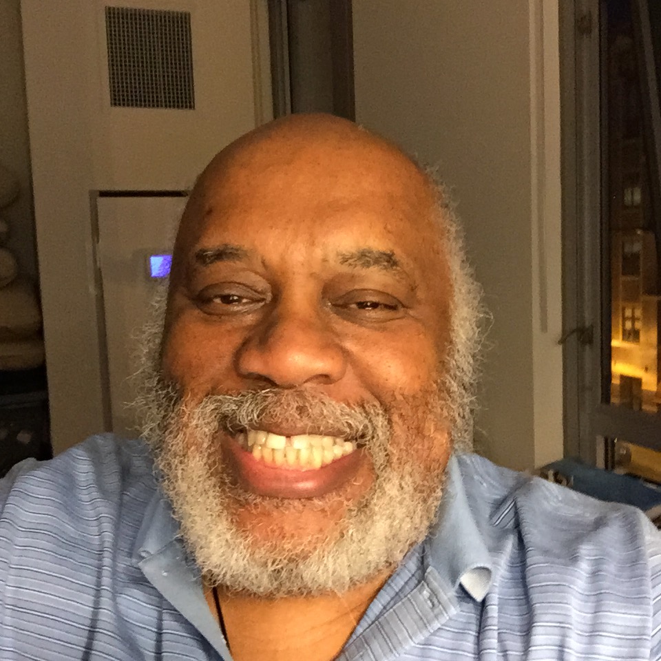 A senior Black man with a white and gray beard smiles at the camera.