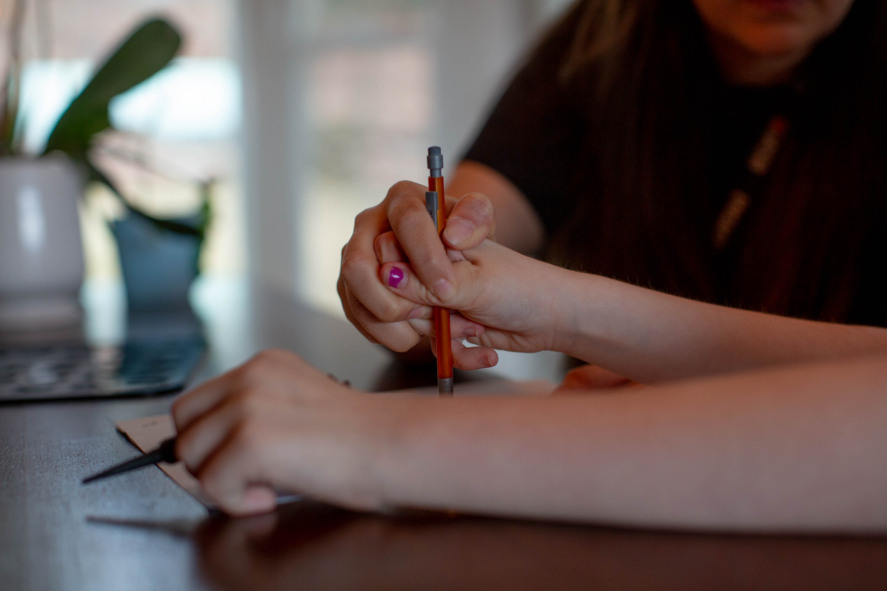A woman holds the hand of a girl as she writes with a mechanical pencil