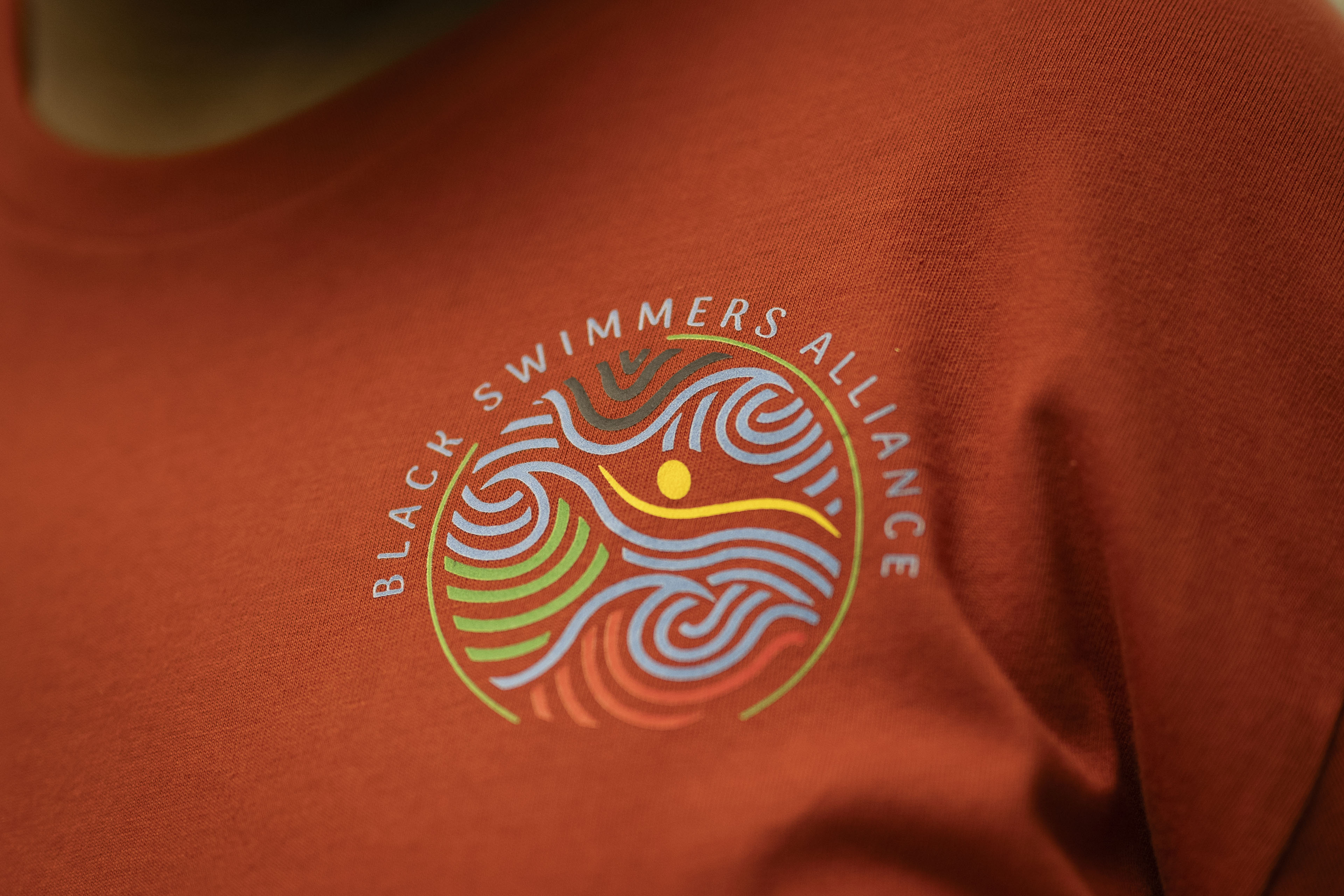 A logo and the name "Black Swimmers Alliance" is seen on an orange t-shirt