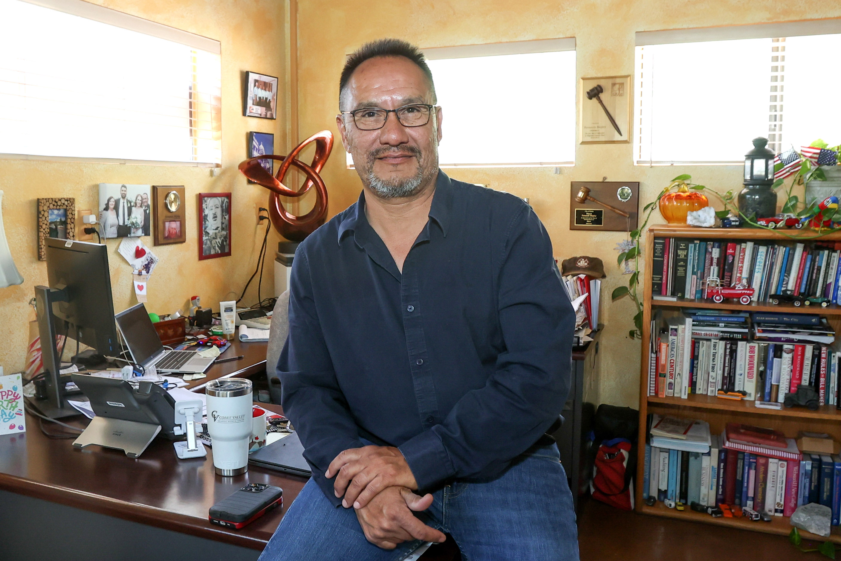 A photo of a man sitting on his desk in an office.