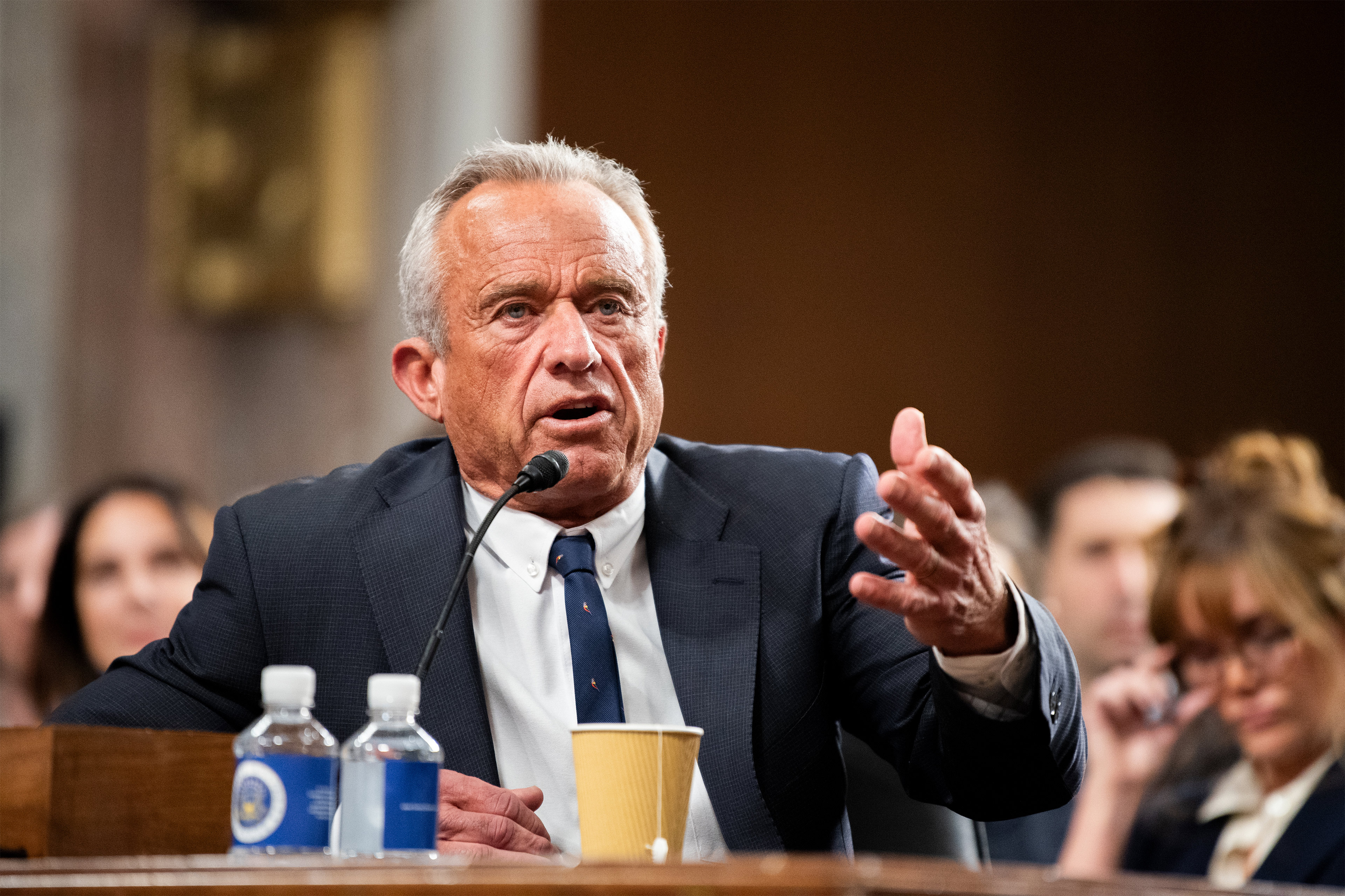 A photo of RFK Jr. speaking at a table in a Senate hearing room.