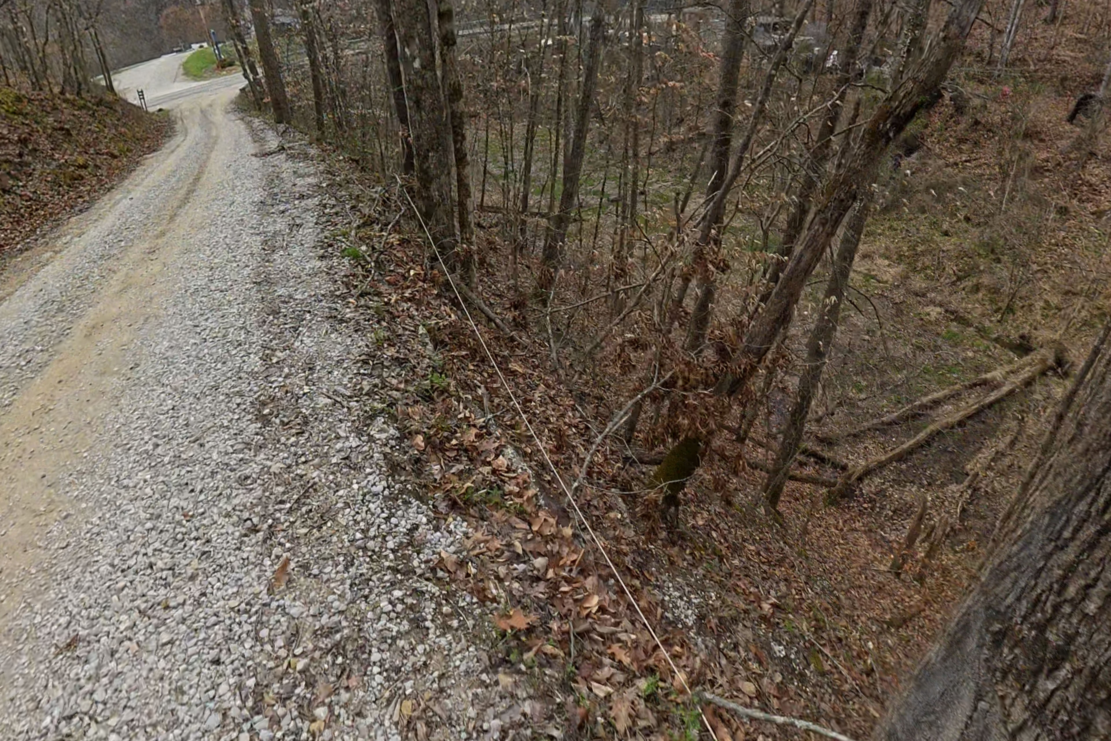 On a gravel tree-lined road, a wire lies on the ground