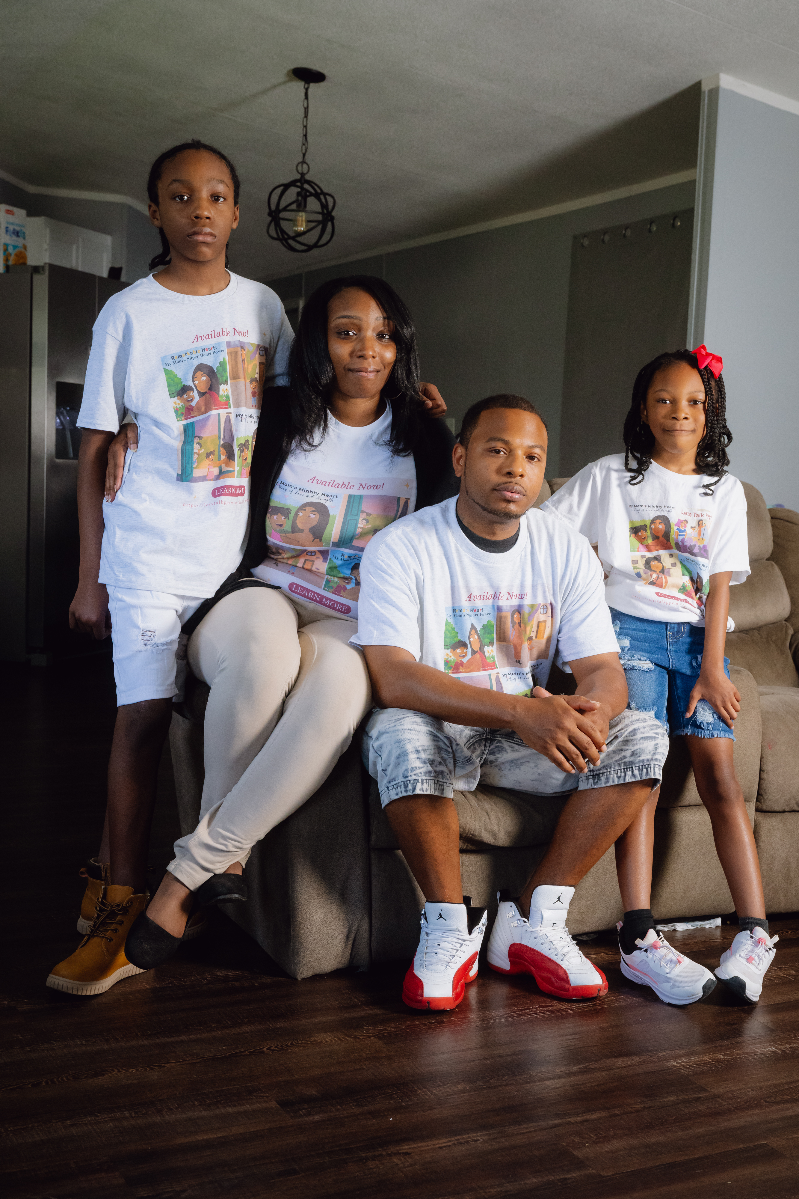 A family portrait taken indoors. From left to right, the adolescent son, mother, father, and young daughter. They are wearing matching T-shirts.