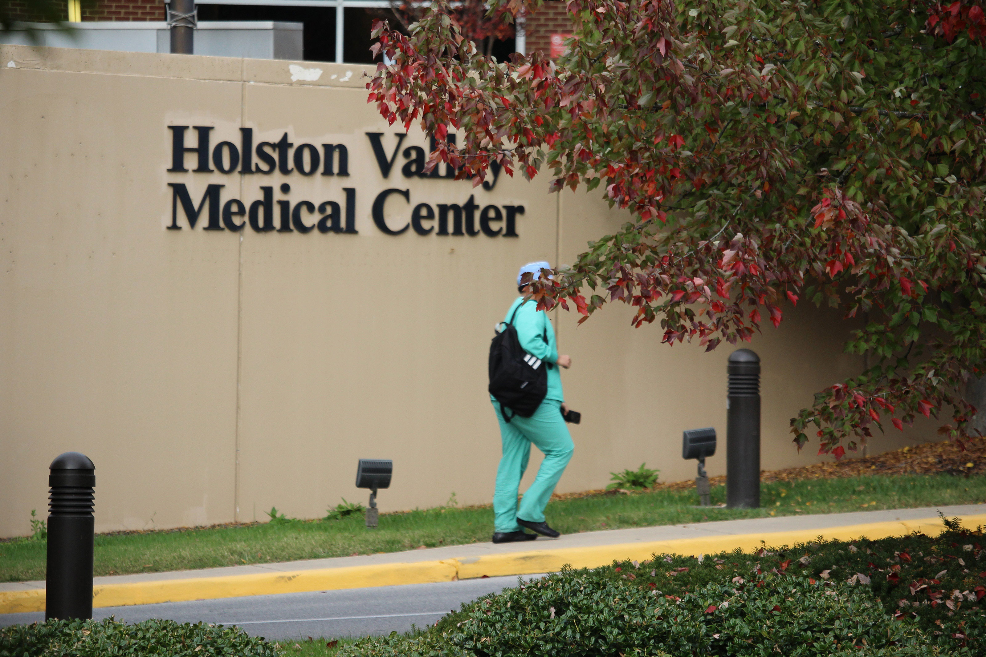 An unidentifiable person in scrubs walks beside a tan wall with a sign reading "Holston Valley Medical Center" on it.