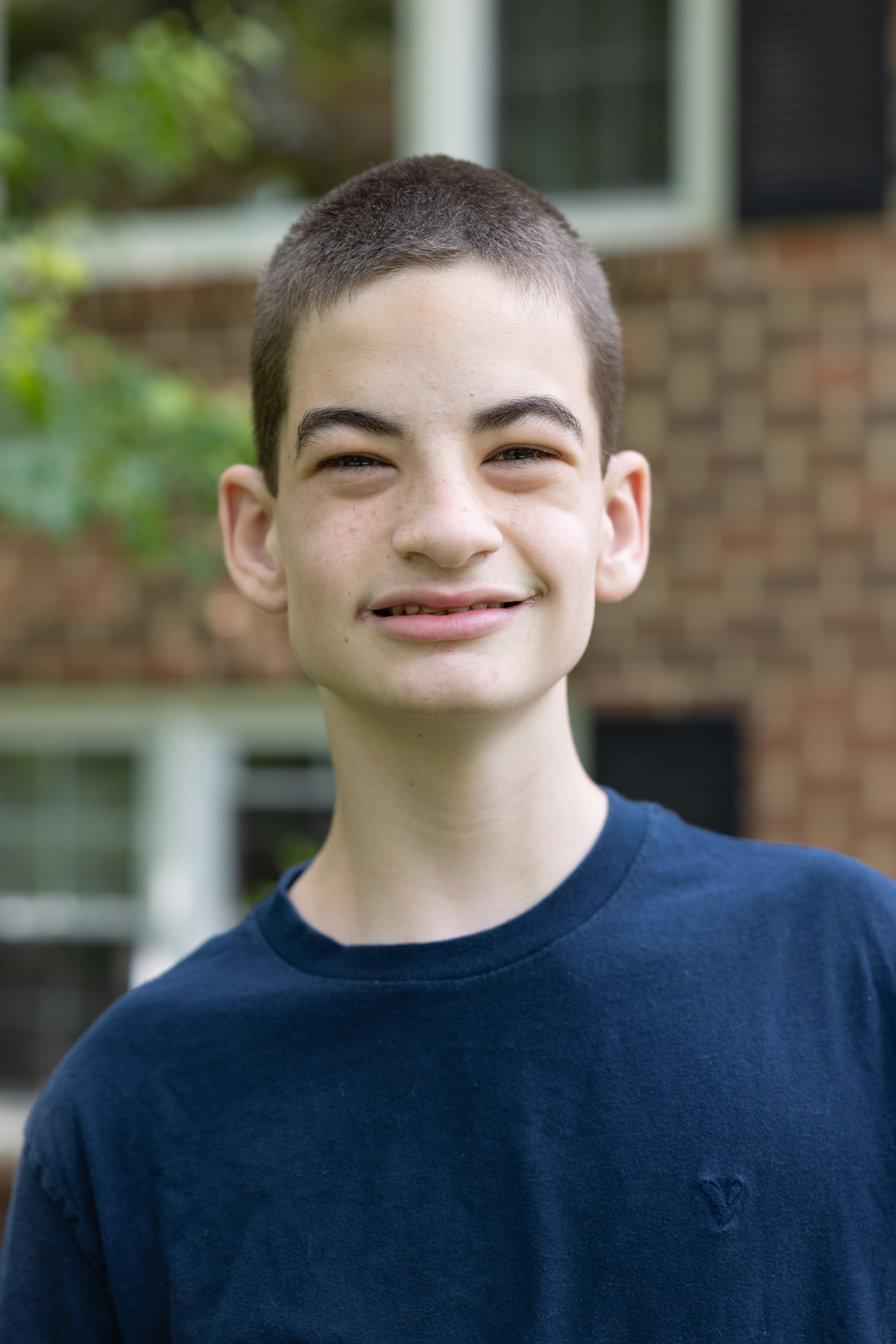 A young man wearing a navy t-shirt and with a shaved head, smiles at the camera.