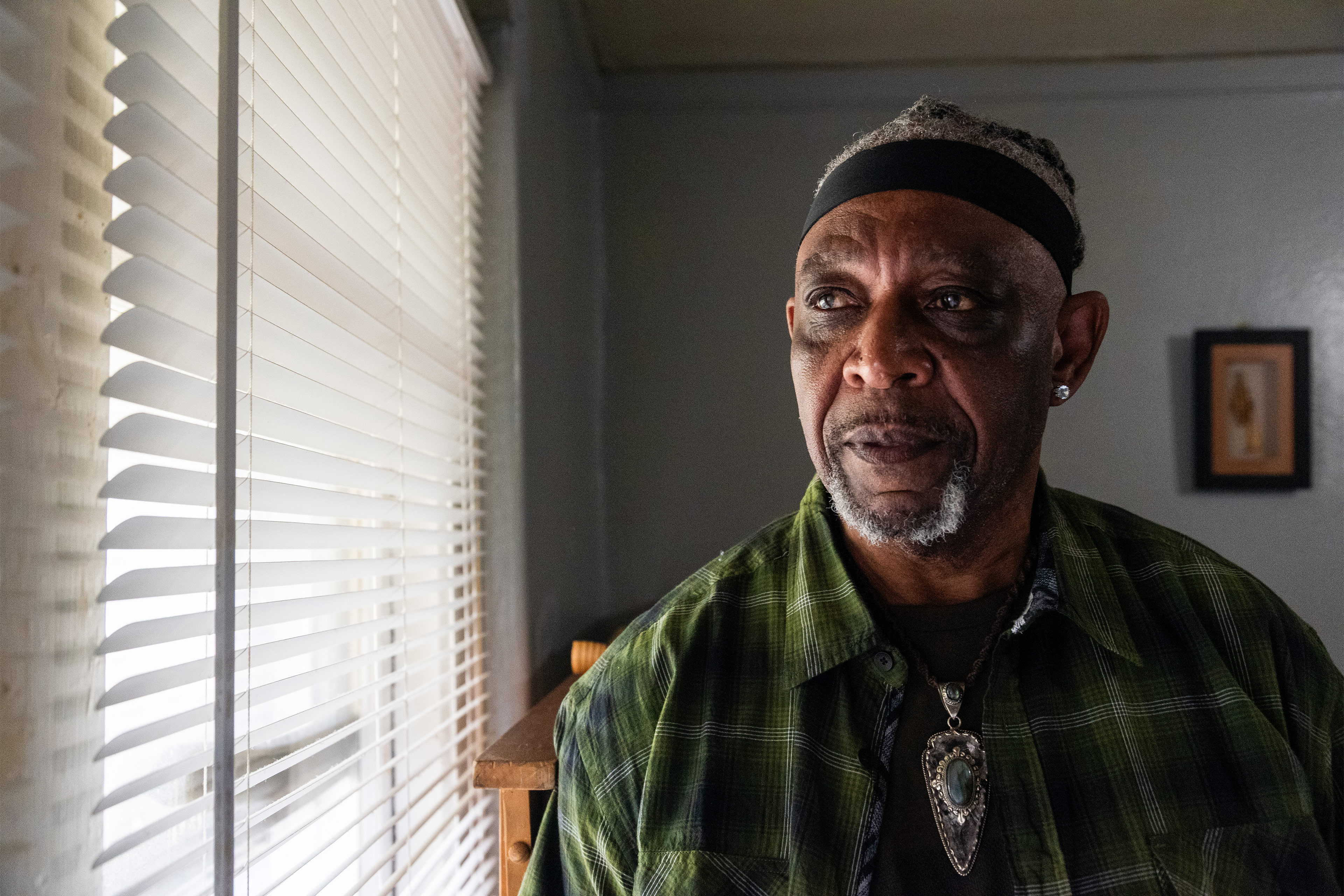 A photo of a Black man posing for a portrait by a window. It is casting dramatic shadows across his face.