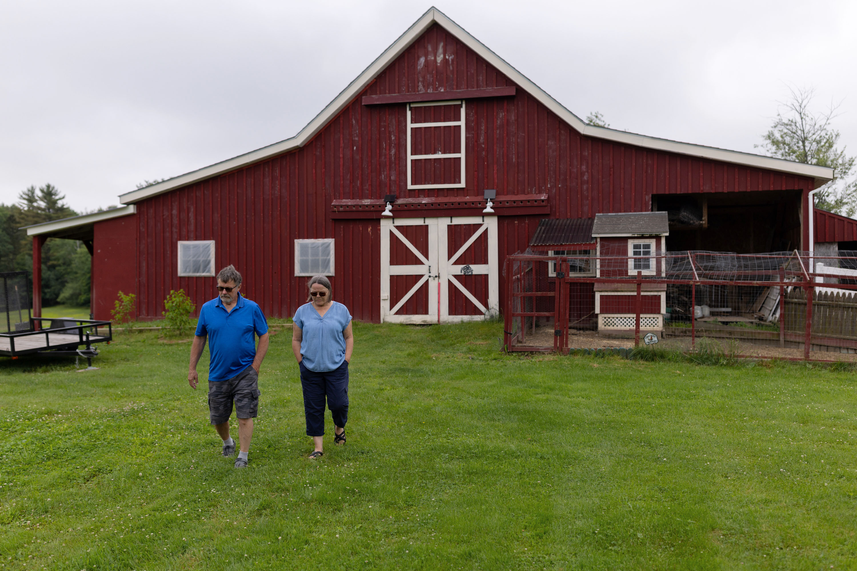 A husband and wife walk towards the camera, and away from a large red barn with white painted doors and windows.