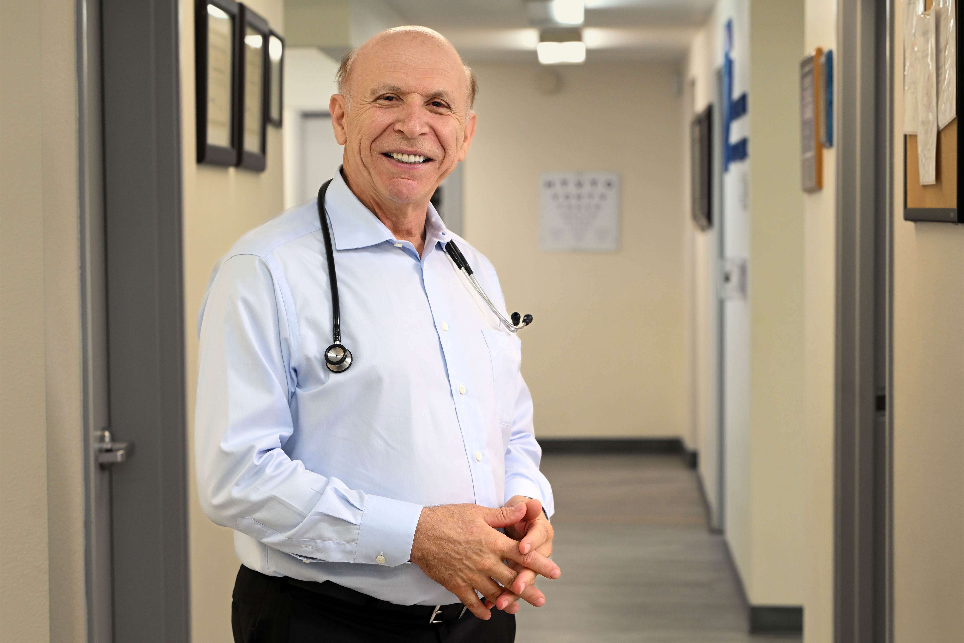 A photo of a doctor posing in his office with a stethoscope draped over his neck.