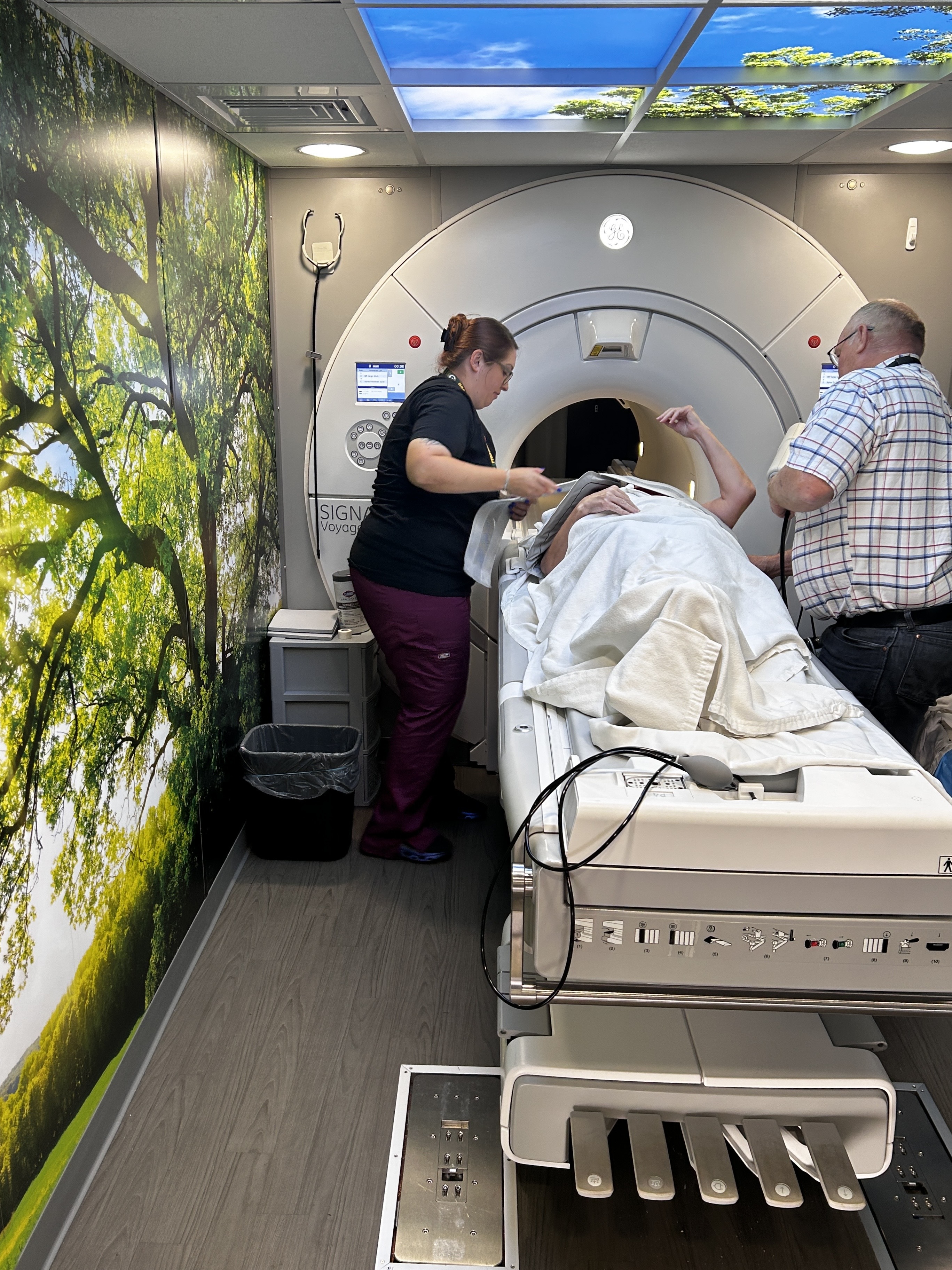 A person attended to by a nurse and another man, lays down in front of an MRI machine