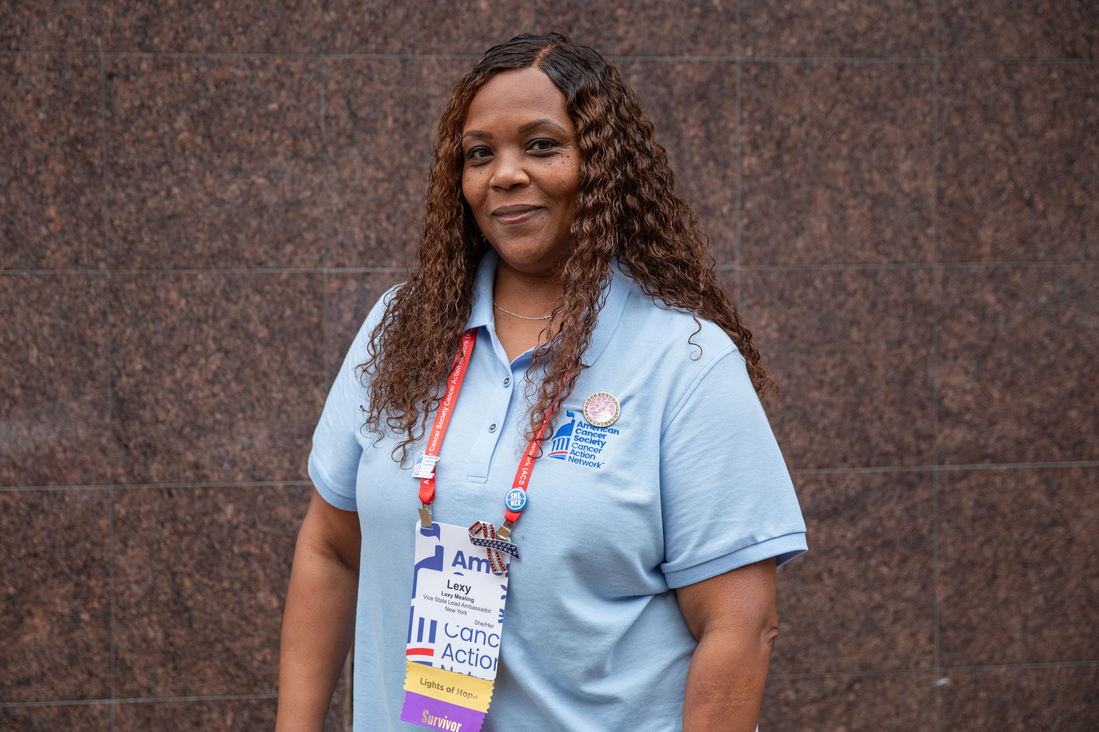 A portrait of a woman wearing a blue shirt standing against a brown background.