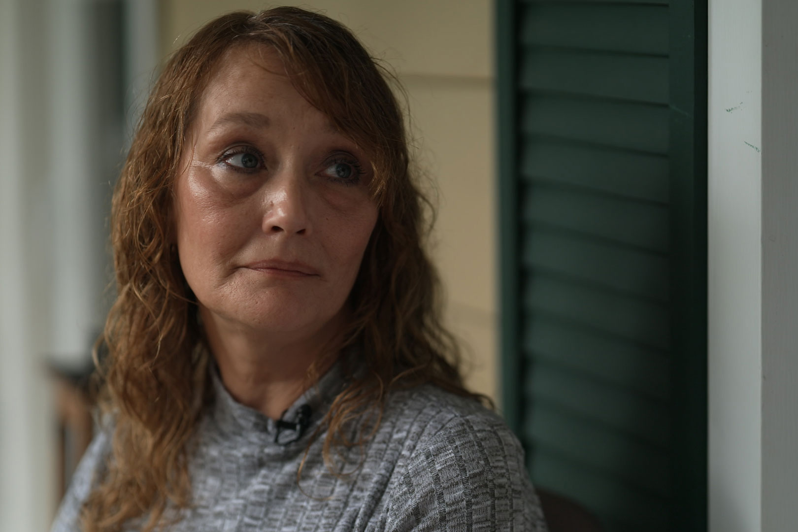 A woman with wavy brown hair and wearing a gray shirt looks off-camera to her left.
